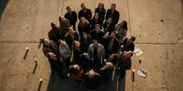 Overhead view of a diverse group of people on a concrete plaza, all looking upwards, captivated by an unseen event, illustrating collective psychological drivers of cultural trends.